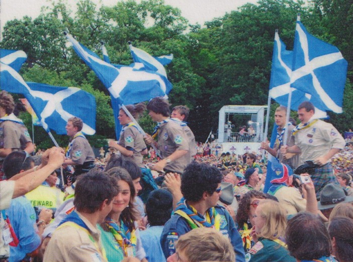 Boys in scout uniforms running and holding flags